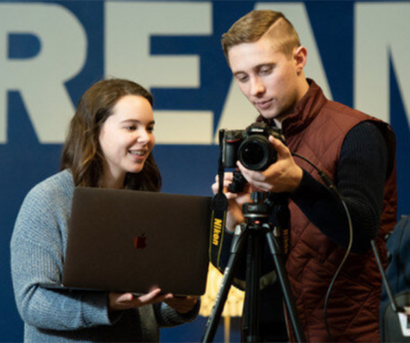 Two people holding a computer and camera, respectively