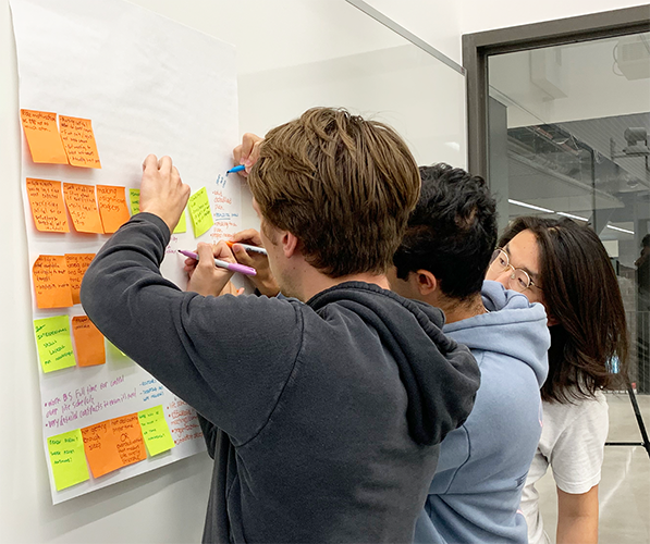 Three people collaborating with sticky notes on a wall