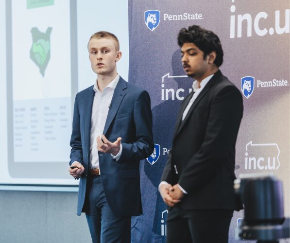 Two students pitching their startup in front of an Inc.U banner