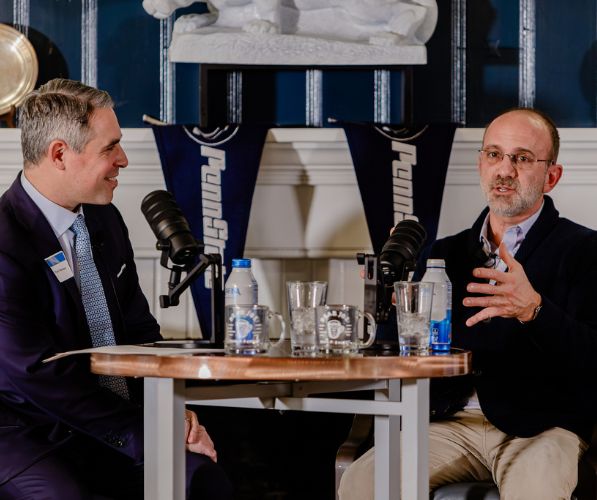 Photo of Ryan Newman and Gary Brandeis sitting at a high top table with podcast microphones recording the Dare to Disrupt Podcast live