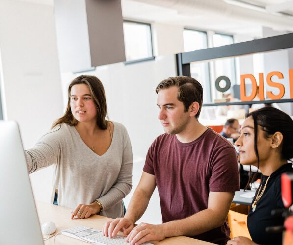 Three individuals collaborating around a computer screen