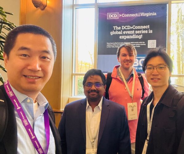 Four individuals stand in front of conference poster, all wearing conference lanyards